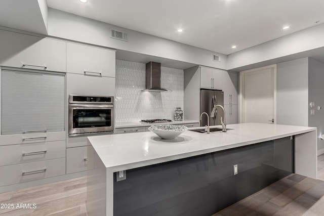 kitchen featuring a sink, stainless steel appliances, light countertops, wall chimney exhaust hood, and modern cabinets