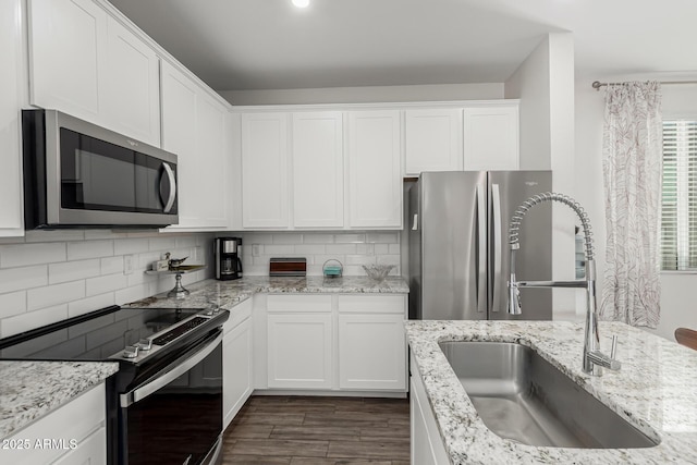 kitchen featuring stainless steel appliances, a sink, white cabinetry, backsplash, and light stone countertops