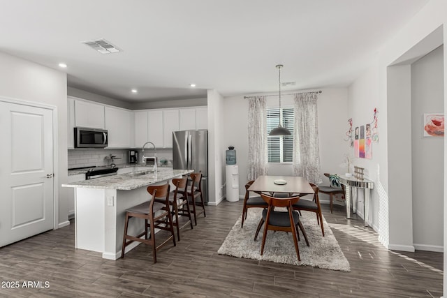 kitchen with visible vents, decorative light fixtures, a kitchen island with sink, stainless steel appliances, and white cabinetry