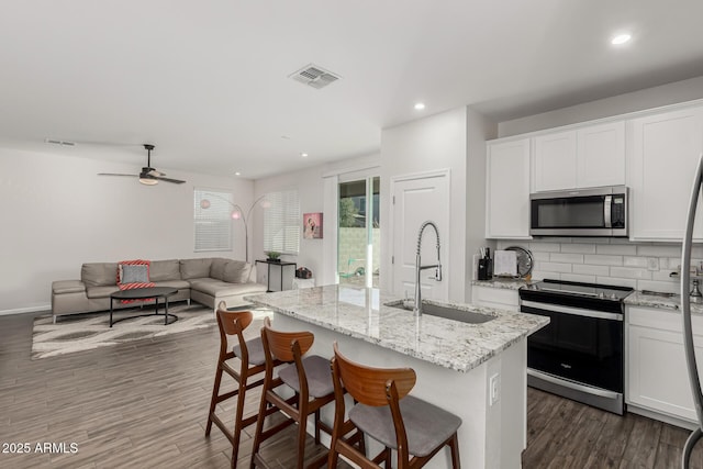 kitchen with a kitchen island with sink, electric stove, stainless steel microwave, and white cabinetry