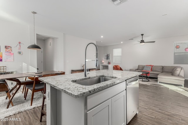 kitchen featuring a kitchen island with sink, a sink, open floor plan, dishwasher, and pendant lighting