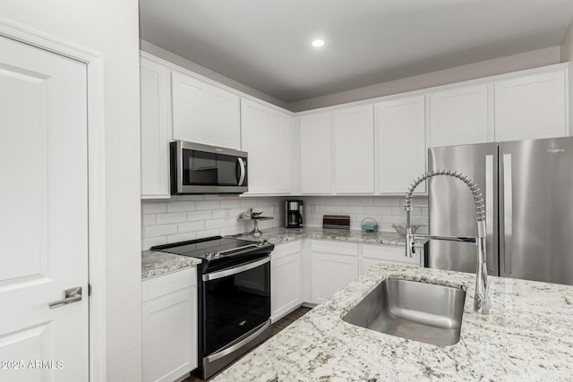 kitchen featuring decorative backsplash, light stone counters, appliances with stainless steel finishes, white cabinetry, and a sink