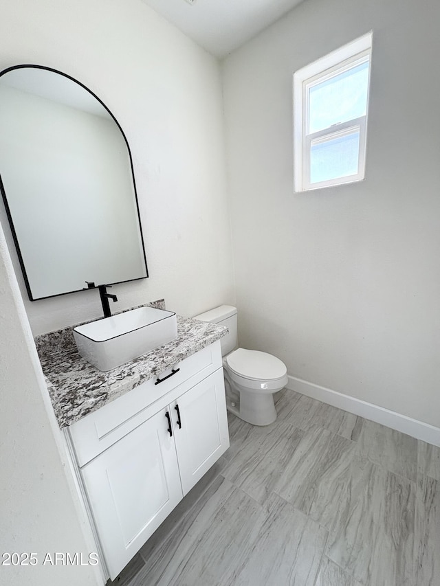 half bath featuring vanity, toilet, and baseboards