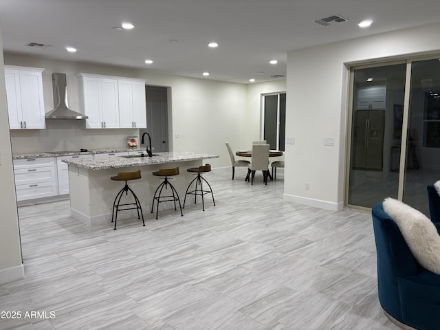 kitchen with an island with sink, wall chimney range hood, visible vents, and a sink