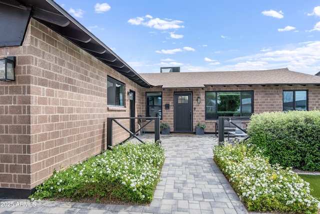 entrance to property with brick siding, roof with shingles, and fence