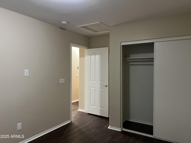 unfurnished bedroom with dark wood-style floors, baseboards, attic access, and a closet
