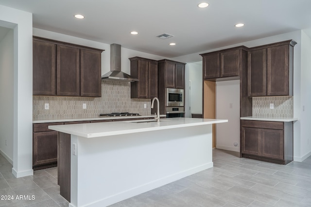 kitchen featuring a kitchen island with sink, sink, wall chimney exhaust hood, and appliances with stainless steel finishes