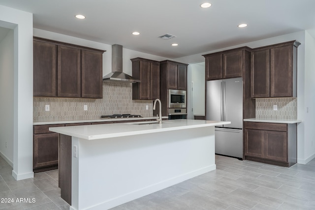 kitchen with appliances with stainless steel finishes, an island with sink, wall chimney exhaust hood, and sink