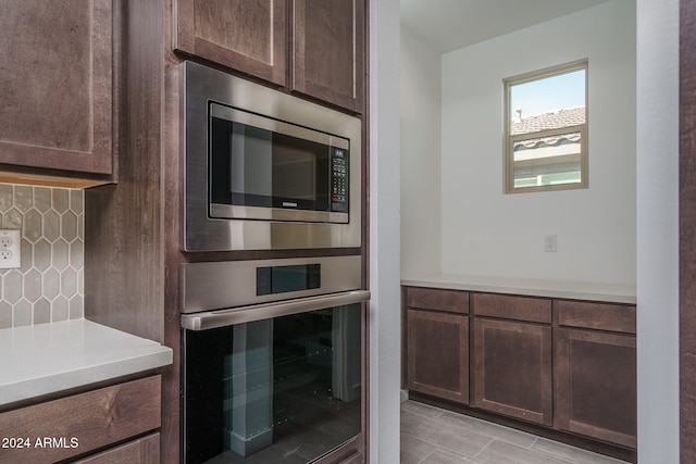 kitchen featuring dark brown cabinets, stainless steel microwave, and backsplash