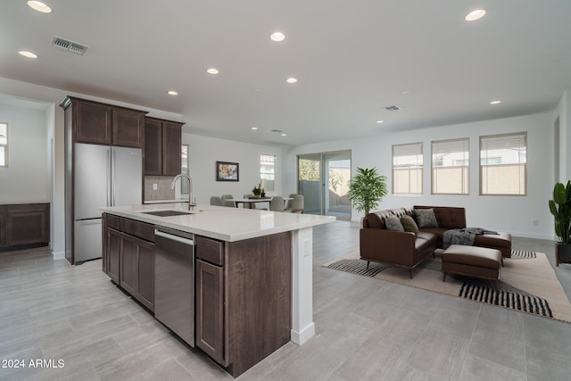 kitchen featuring backsplash, a center island with sink, refrigerator, sink, and stainless steel dishwasher