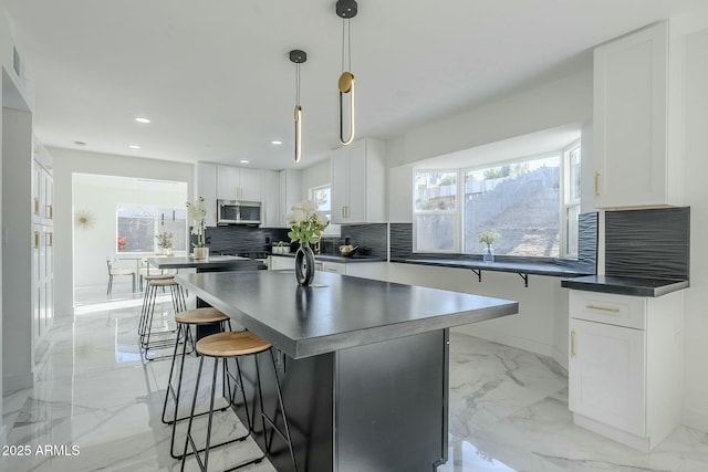 kitchen featuring white cabinetry, backsplash, a kitchen breakfast bar, hanging light fixtures, and a center island