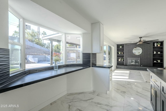 kitchen featuring ceiling fan, plenty of natural light, a brick fireplace, and white cabinets