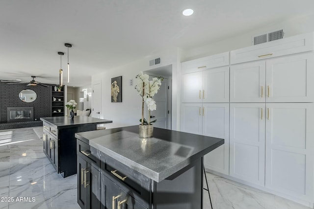 kitchen with pendant lighting, a fireplace, white cabinets, a center island, and ceiling fan