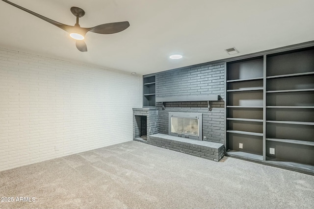 unfurnished living room with brick wall, built in features, a fireplace, carpet, and ceiling fan