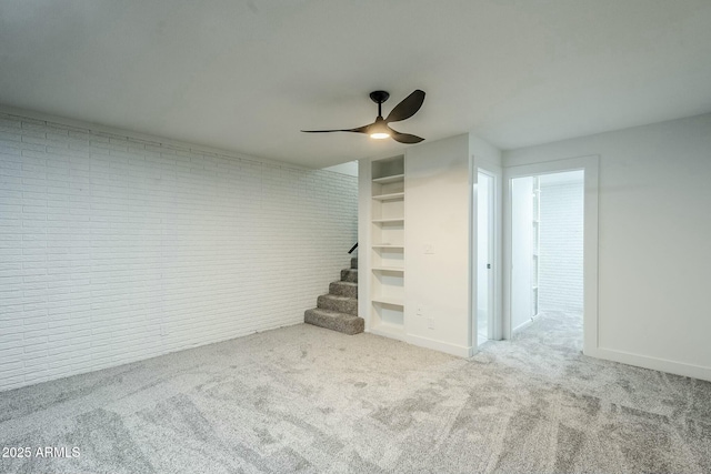 basement with brick wall, light colored carpet, ceiling fan, and built in shelves