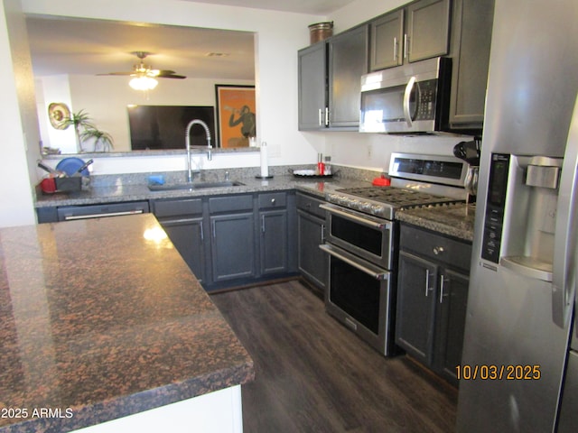 kitchen with a ceiling fan, dark stone counters, dark wood-style flooring, a sink, and appliances with stainless steel finishes