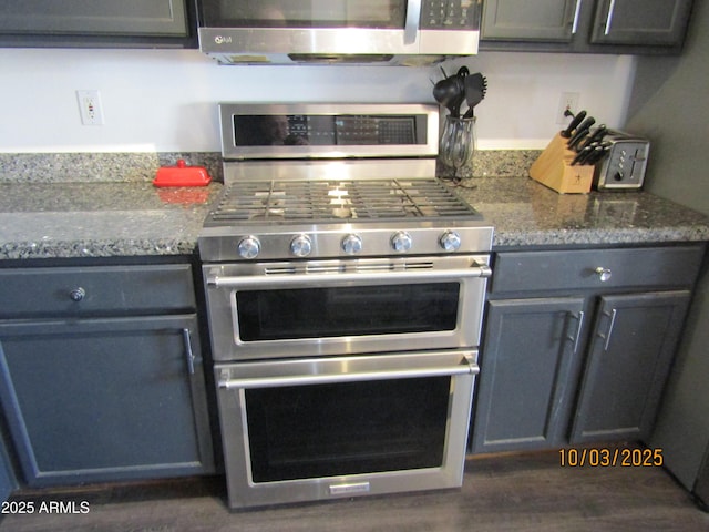 kitchen with dark stone countertops, stainless steel appliances, dark wood finished floors, and gray cabinets