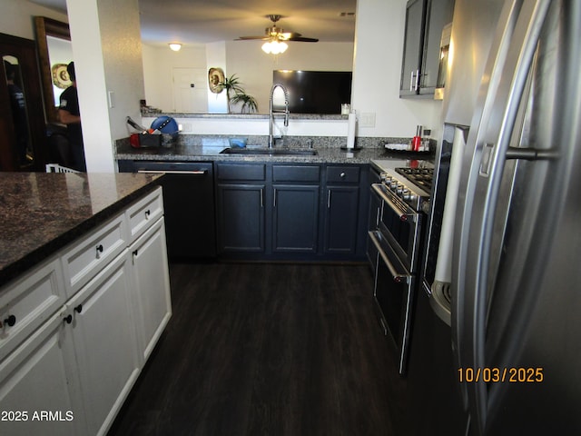 kitchen featuring a ceiling fan, dark wood finished floors, dark stone counters, a sink, and stainless steel appliances