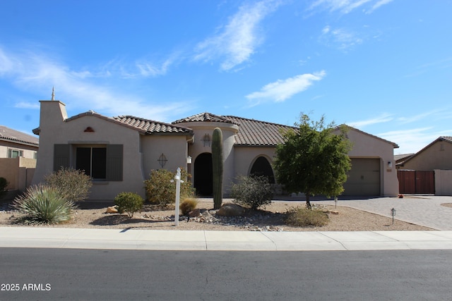 mediterranean / spanish-style house with an attached garage, a tile roof, decorative driveway, and stucco siding