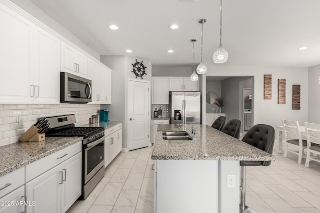 kitchen with a kitchen island with sink, a sink, a kitchen breakfast bar, appliances with stainless steel finishes, and white cabinets