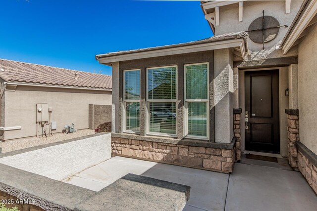doorway to property featuring a patio area, stone siding, stucco siding, and a tiled roof