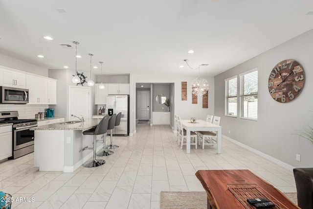kitchen with an inviting chandelier, a sink, decorative backsplash, stainless steel appliances, and a kitchen bar