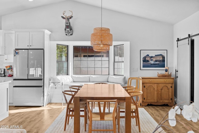 dining space featuring a barn door, light hardwood / wood-style floors, and vaulted ceiling