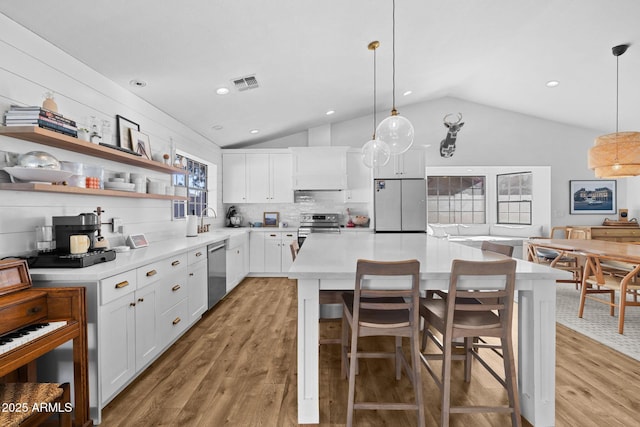 kitchen with tasteful backsplash, stainless steel appliances, pendant lighting, white cabinets, and lofted ceiling