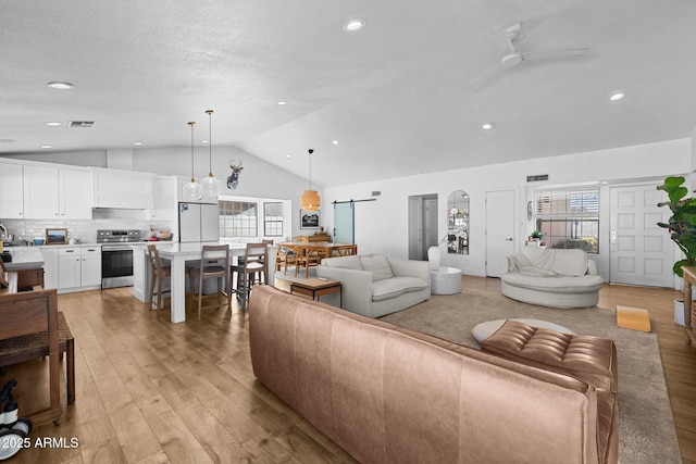 living room featuring a barn door, ceiling fan, light hardwood / wood-style floors, and vaulted ceiling