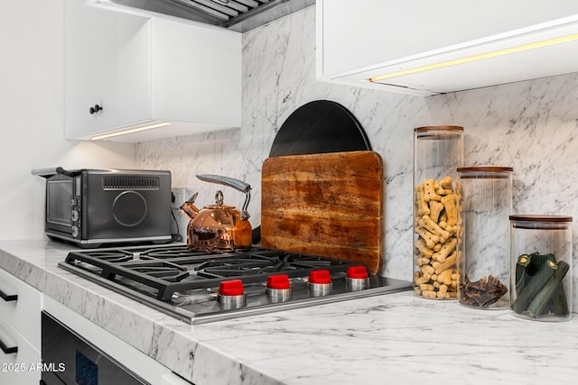 interior details featuring white cabinetry, tasteful backsplash, wall chimney exhaust hood, and stainless steel gas stovetop