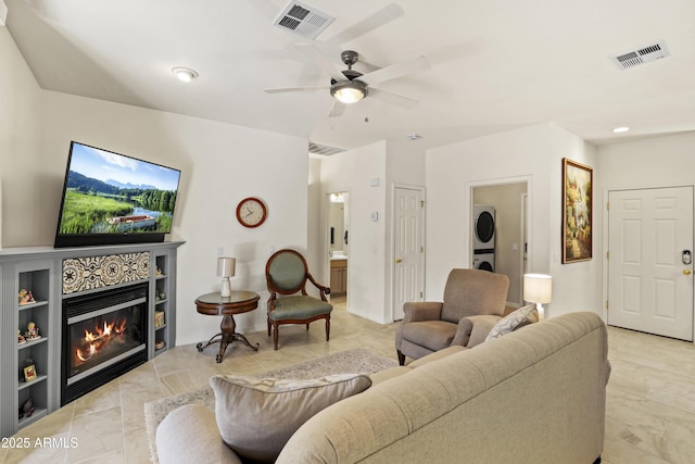 living room featuring a ceiling fan, visible vents, stacked washer and clothes dryer, and a tile fireplace