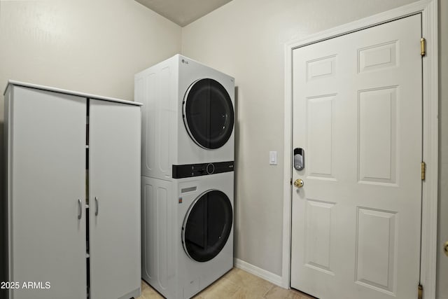 clothes washing area with baseboards, laundry area, stacked washer and dryer, and light tile patterned flooring