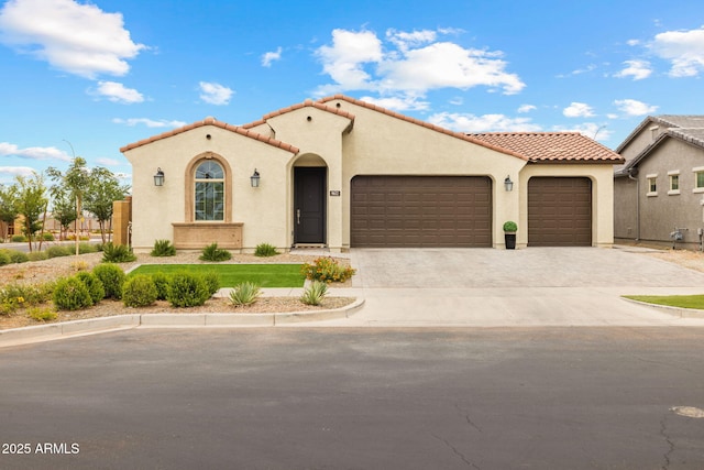 mediterranean / spanish-style home featuring a garage, a tiled roof, stucco siding, and driveway