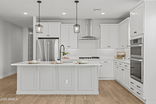 kitchen featuring wall chimney range hood, appliances with stainless steel finishes, light countertops, light wood-style flooring, and recessed lighting