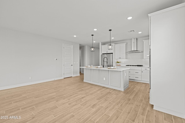 kitchen with wall chimney exhaust hood, light countertops, a center island with sink, light wood-style floors, and recessed lighting