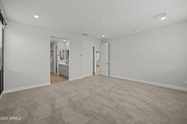 unfurnished bedroom featuring light carpet, recessed lighting, baseboards, and ensuite bathroom