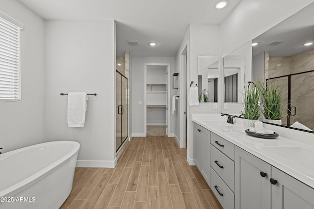 full bathroom with a stall shower, a soaking tub, wood finished floors, double vanity, and baseboards