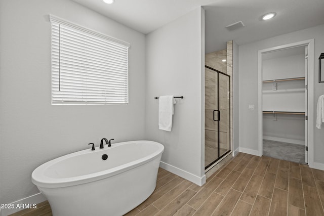 full bath featuring a walk in closet, a stall shower, wood finished floors, a freestanding tub, and baseboards