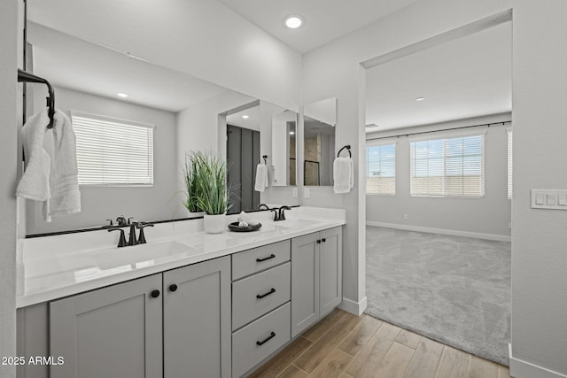 bathroom with baseboards, double vanity, wood finished floors, and recessed lighting