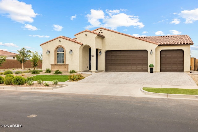 mediterranean / spanish-style house with an attached garage, stucco siding, decorative driveway, and a tiled roof