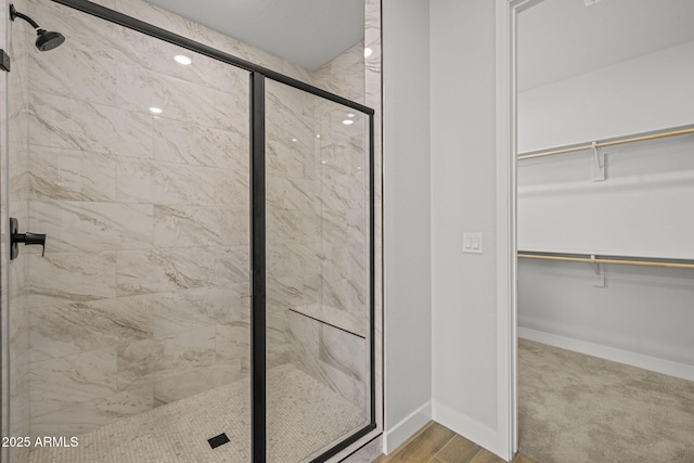 full bathroom with a stall shower, a spacious closet, and baseboards