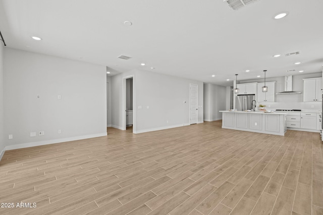 unfurnished living room featuring baseboards, light wood-type flooring, recessed lighting, and a sink