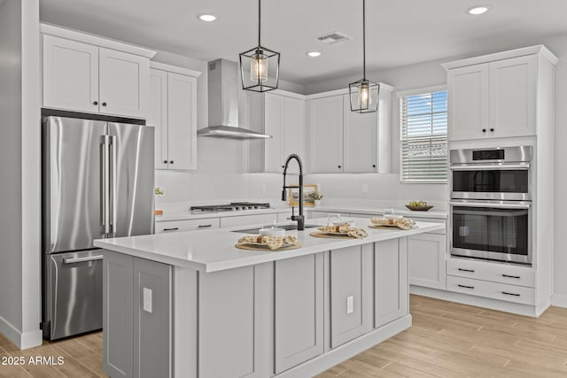 kitchen with stainless steel appliances, wall chimney range hood, light countertops, light wood finished floors, and a sink