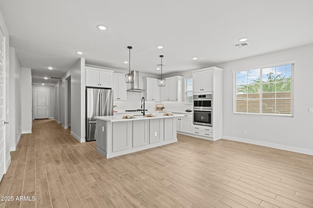 kitchen featuring stainless steel appliances, wall chimney exhaust hood, light countertops, baseboards, and light wood finished floors