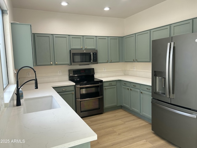 kitchen with appliances with stainless steel finishes, sink, green cabinetry, and light hardwood / wood-style flooring