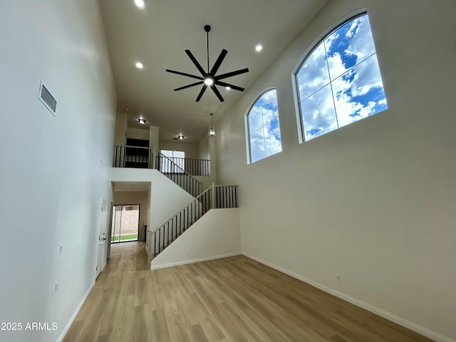 unfurnished living room with light wood-type flooring, ceiling fan, and a towering ceiling