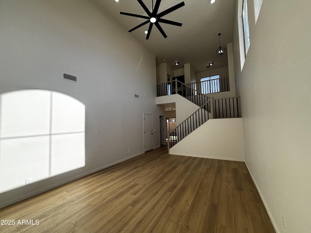 unfurnished living room featuring ceiling fan, a high ceiling, and hardwood / wood-style flooring