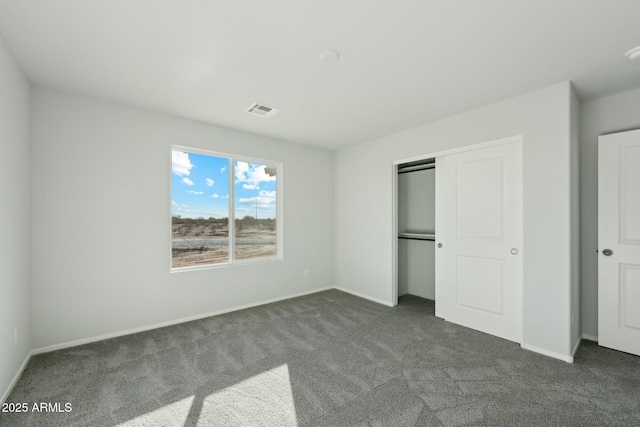 unfurnished bedroom featuring baseboards, visible vents, dark colored carpet, and a closet