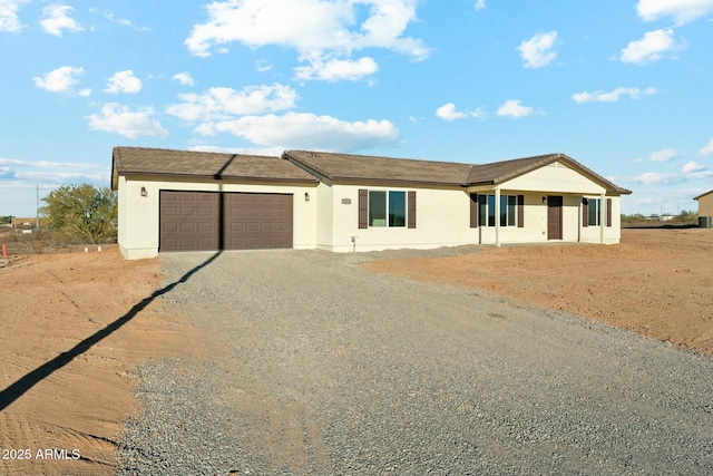 single story home featuring a garage, gravel driveway, and stucco siding