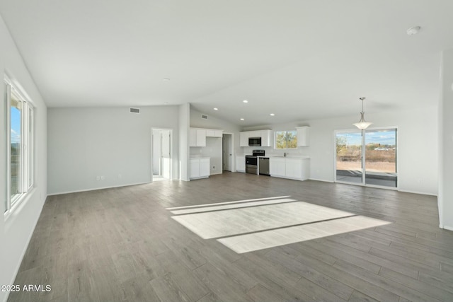 unfurnished living room with lofted ceiling, recessed lighting, visible vents, wood finished floors, and baseboards